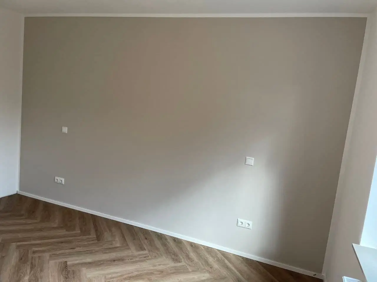 Große, gleichmäßig gestrichene Wandfläche in warmem Grauton mit sauberem Anschluss an Decke und Boden