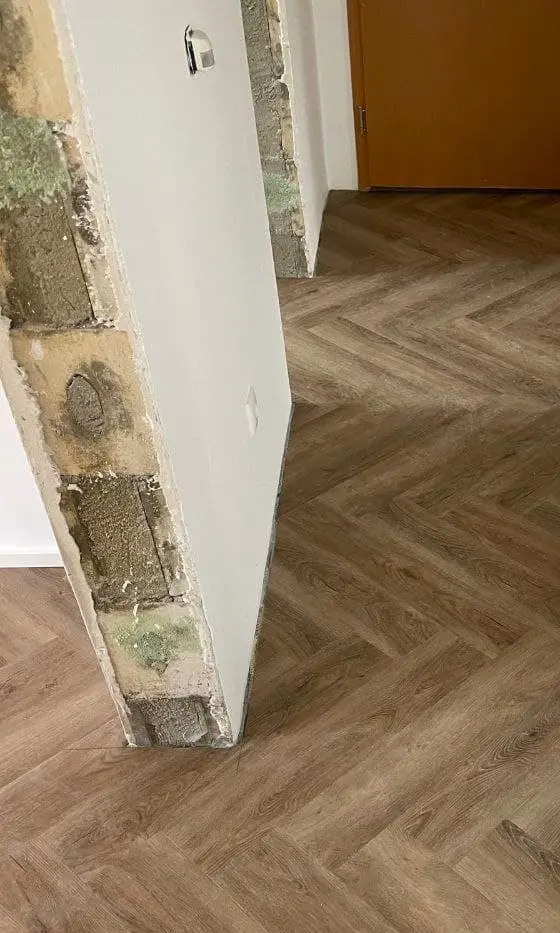 Geöffnete Wandlaibung mit freiliegendem Mauerwerk und Mörtelfugen, daneben eine bereits fertig gespachtelte Wandfläche
